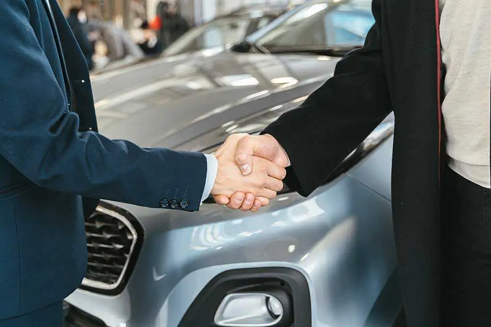 Autokaufvertrag online – Handshake zwischen Käufer und Verkäufer Autokaufvertrag online: Käufer und Verkäufer geben sich vor dem Auto die Hand